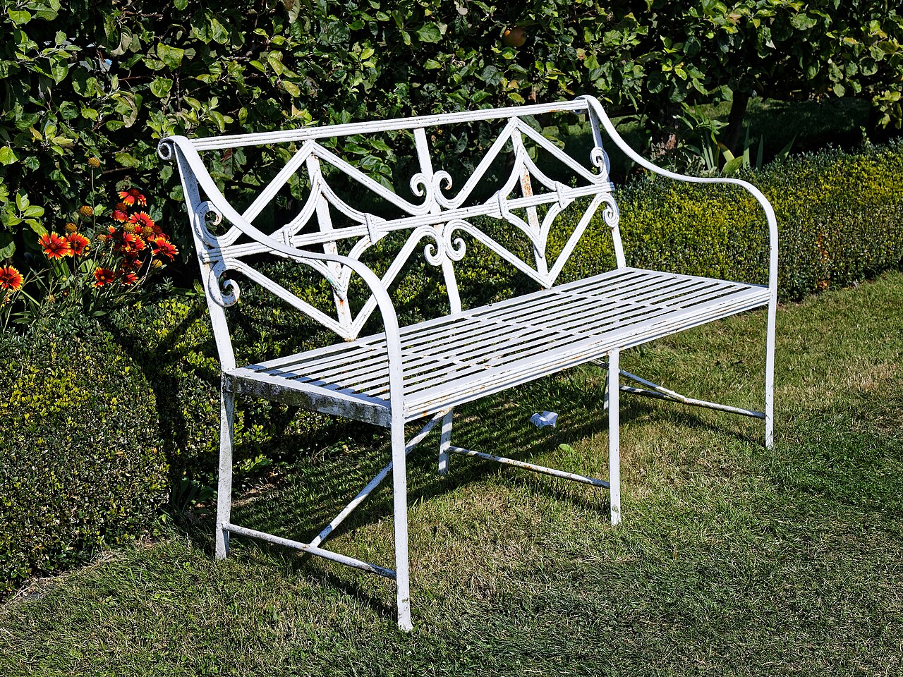 Banc en fer forgé dans un jardin anglais — structure en métal ouvragé, assise et dossier à volutes
